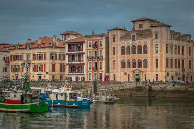 Boats moored in river by buildings in city against sky