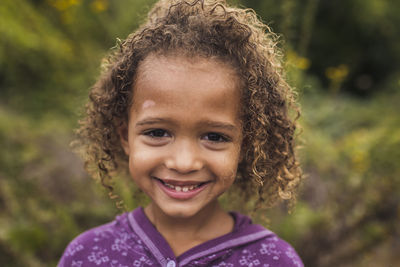 Close-up portrait of happy girl with curly hair standing in park