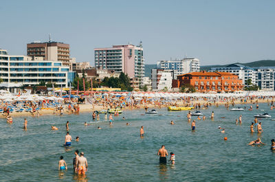 Group of people swimming in the sea against built structures
