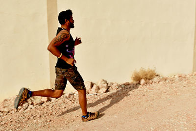 Side view of young man running by building