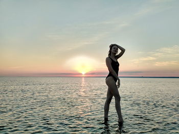 Woman standing at beach against sky during sunset