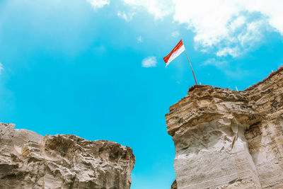 Low angle view of flag on rock formation against sky