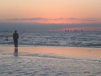 Silhouette man walking on shore at beach against sky during sunset