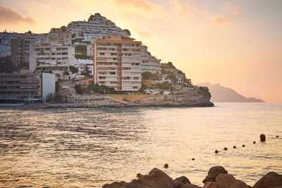 Buildings by sea against sky during sunset