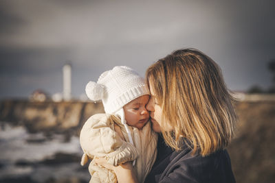 A woman is holding a baby near a lighthouse on the pacific coast