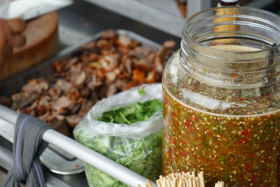 Closeup spicy sauce in the glass jar with blurred stewed pork and coriander in background