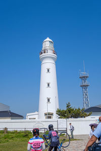 People on lighthouse by building against clear blue sky