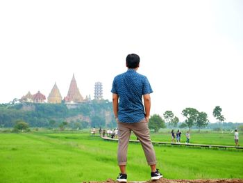 Rear view of man standing on field against clear sky