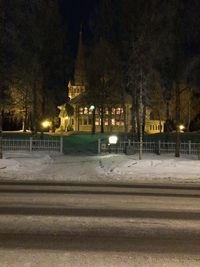 Illuminated road by building during winter at night