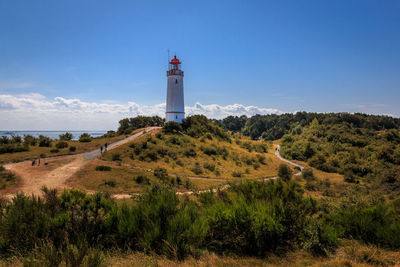 Lighthouse on field by building against sky