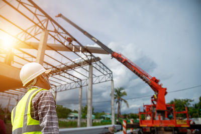 An asian foreman standing in control of a crane driver is steering a crane to install metal sheets