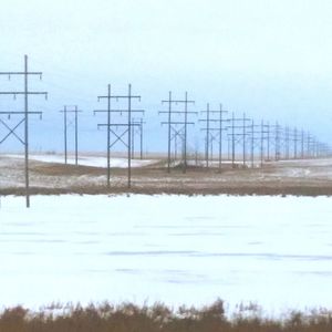 Electricity pylon on snow covered landscape against sky