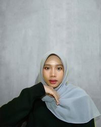 Portrait of young woman in hijab standing against wall