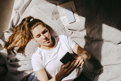 Directly above shot of young woman using smart phone while lying on bed at home