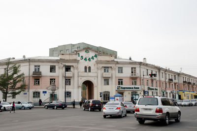 Vehicles on road by buildings against clear sky