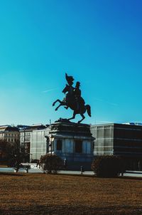 Statue against building in city against clear blue sky