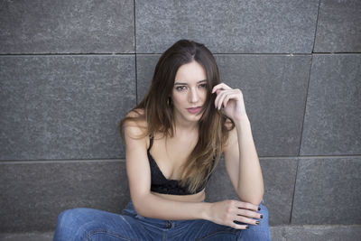 Portrait of young woman sitting against wall