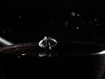 Close-up of drop falling on glass against black background