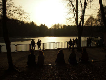 Silhouette people by railing against sky during sunset