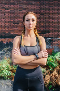 Sportswoman with crossed arms looking camera posing in front of a brick wall