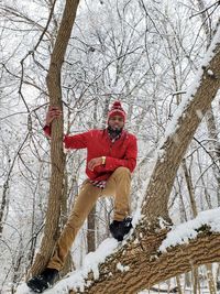 Portrait of man standing on tree in forest during winter