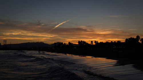 Silhouette city by sea against sky during sunset