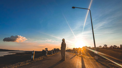 Rear view of man walking on road against sky during sunset