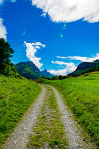 Scenic view of road amidst field against blue sky