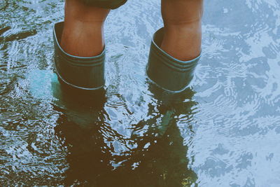 Low section of person wearing rubber boots while standing in water