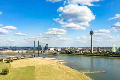 View of city buildings by river against sky