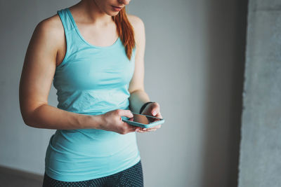 Midsection of woman using mobile phone while standing against wall