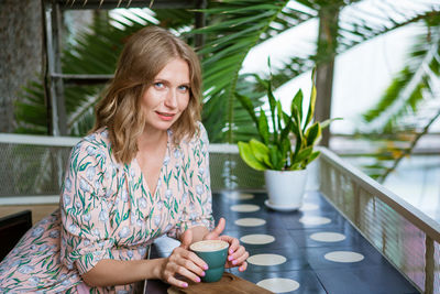 Happy smiling middle aged woman sitting in cafeteria holding coffee mug looking