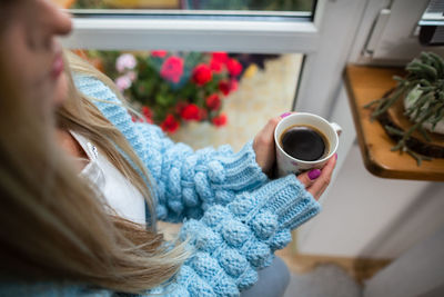 A woman warms her frozen hands against a mug of hot coffee.