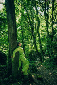 Woman in green dress leaning on tree trunk at forest