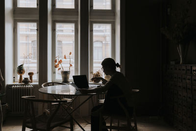 Non-binary person examining financial bills while sitting at table in living room