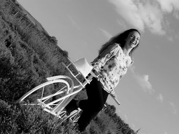 Low angle view of smiling woman standing by bicycle against sky