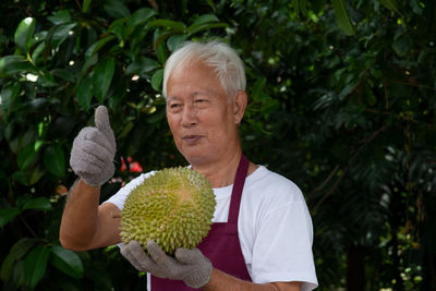 Smiling man showing thumbs up while holding durian