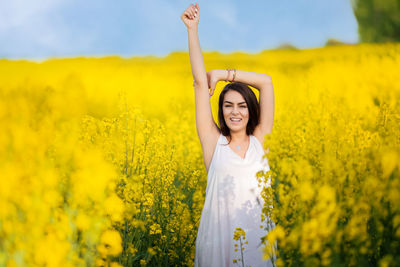 Happy young beautiful woman enjoying a carefree summer day in a yellow flower field