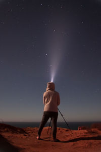 Rear view of man standing on beach against sky at night