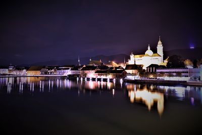 Illuminated buildings by river against sky at night