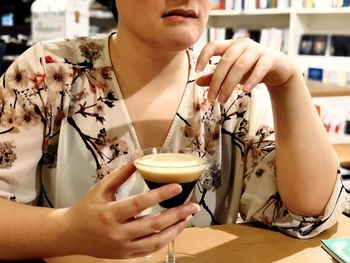 Midsection of woman drinking glass at table