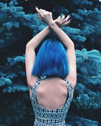 Rear view of woman with arms raised while standing against tree