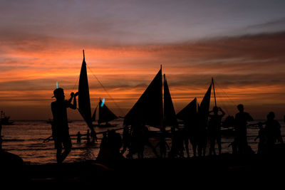 Silhouette people by boat against sky during sunset