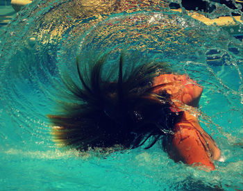 Side view of woman tossing hair in turquoise swimming pool