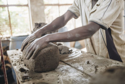 Midsection of worker kneading clay at table in workshop