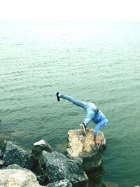 Man doing handstand on rock by sea