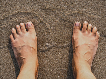 Low section of man standing on sand