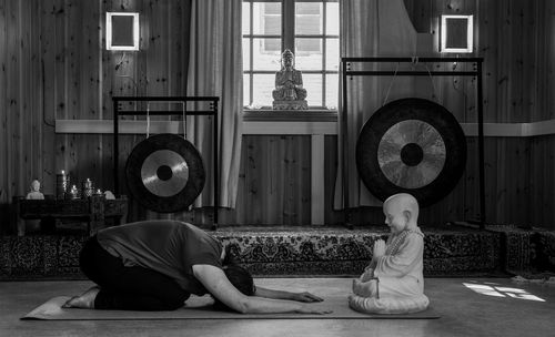 Side view of woman bowing to buddha statue indoors