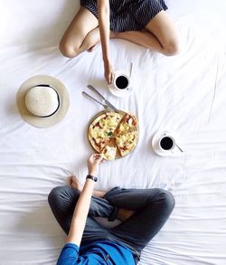 Directly above shot of man and woman with pizza and coffee cups on bed