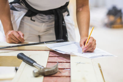 Midsection of young female trainee drawing on paper at workbench in illuminated workshop